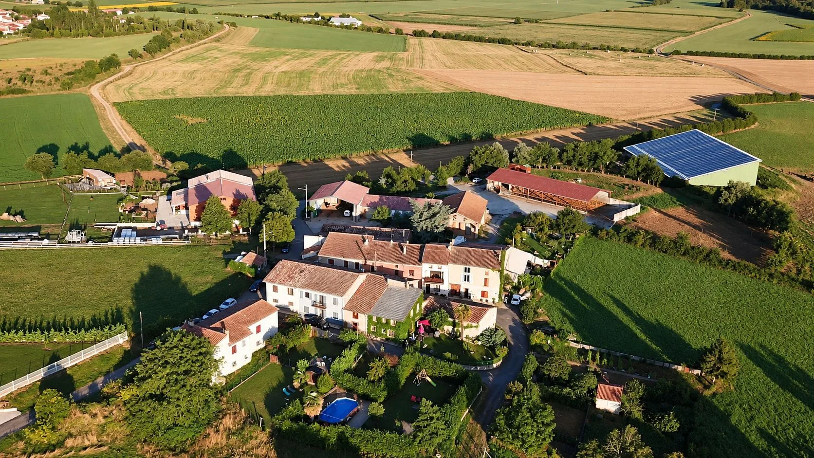 Vue aérienne du hameau de Campserdou au milieu des champs et des prairies, avec un hangar à toit de panneaux solaires.
