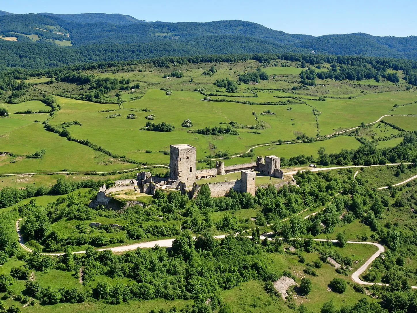 Vue aérienne du château de Puivert, sa tour carrée et ses remparts, entourés de prairies et de forêts.