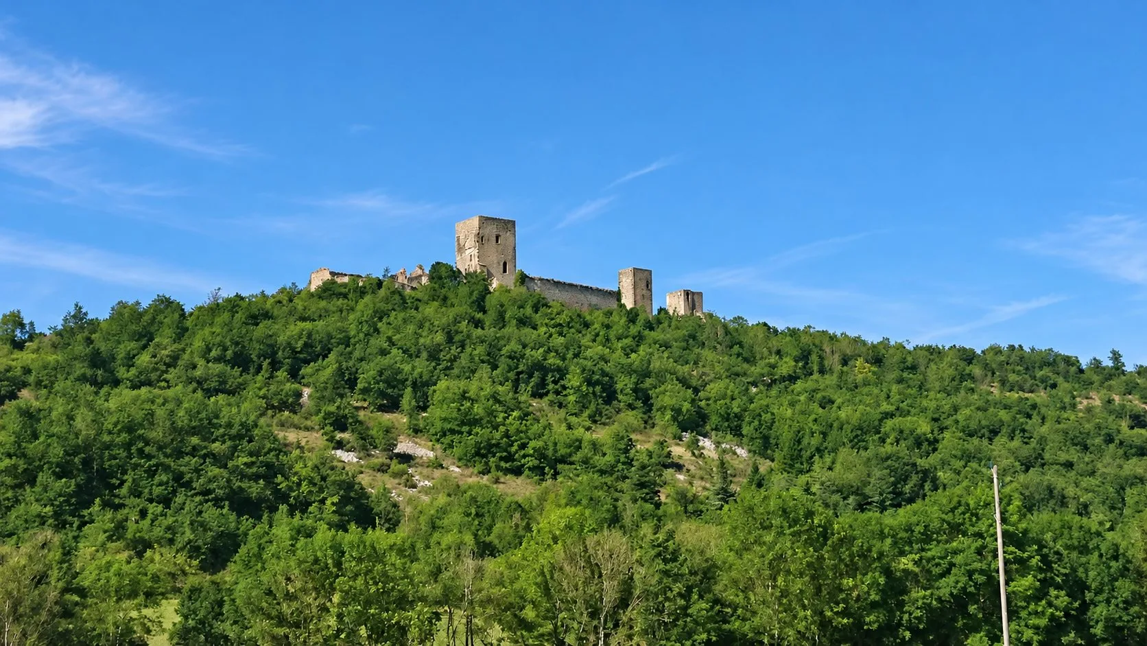 Le château de Puivert au sommet d'une colline boisée, sous un ciel bleu.
