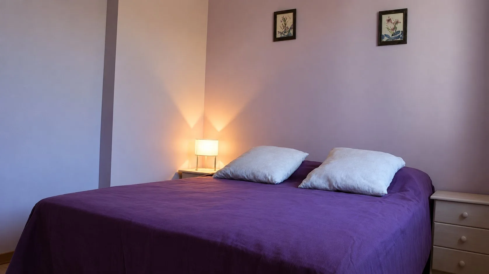 Chambre du gîte Balcon avec un lit double violet, deux oreillers blancs et une lampe de chevet.