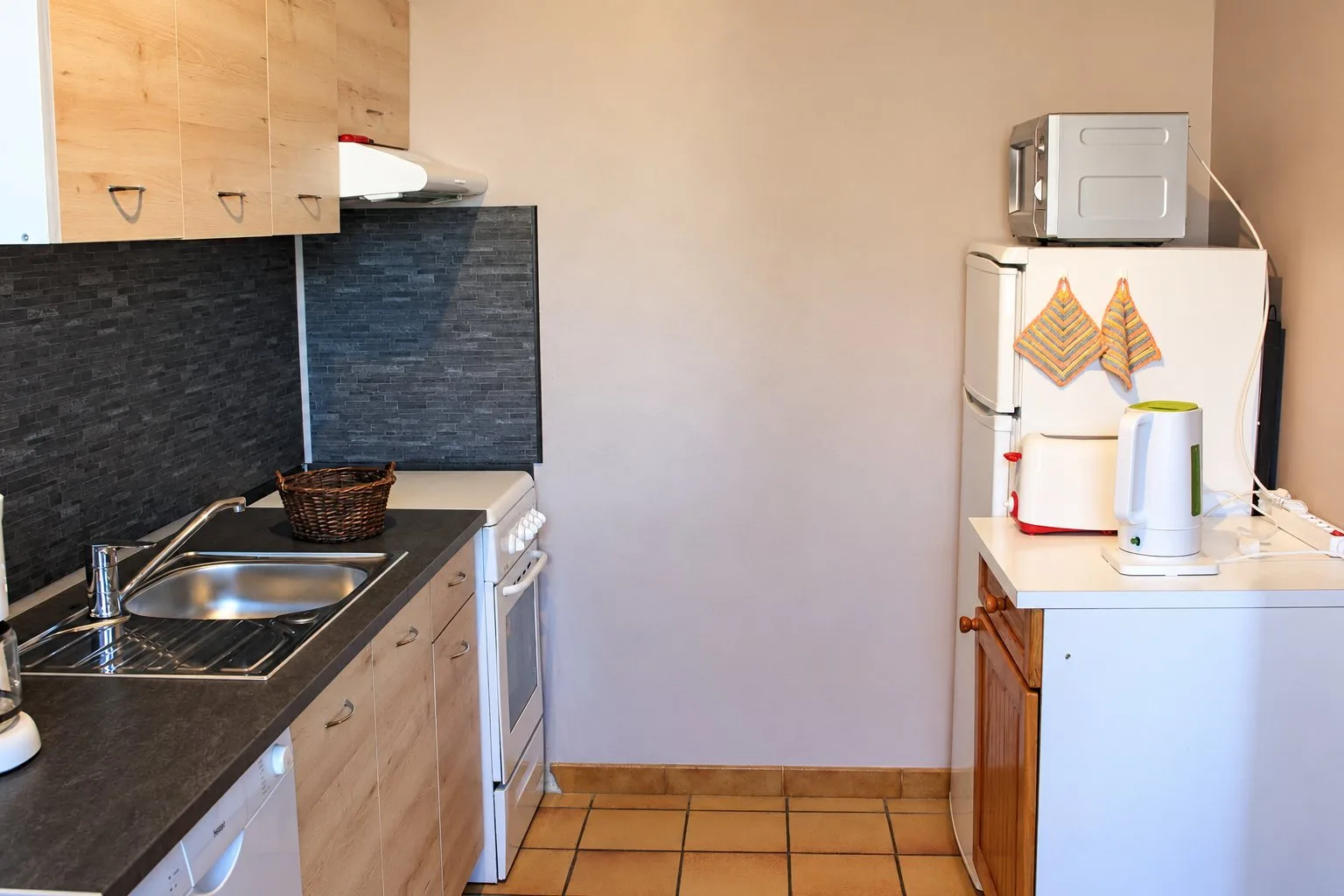Cuisine du gîte Balcon avec évier, plan de travail sombre, meubles en bois clair, micro-ondes et bouilloire.