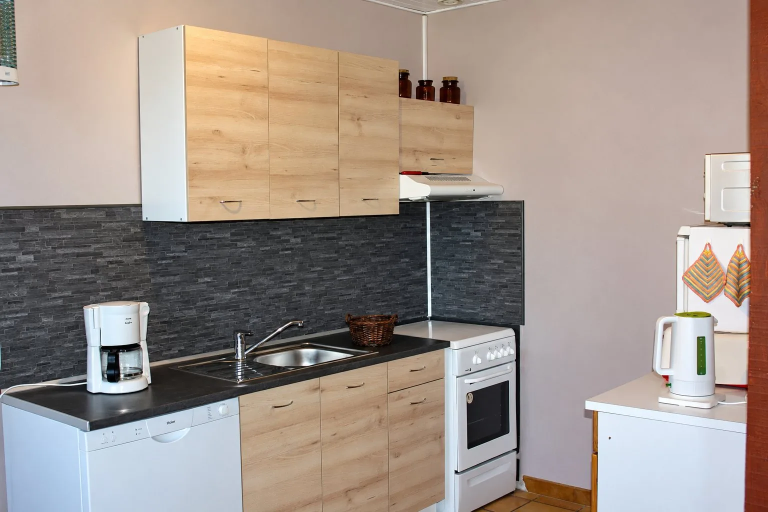 Cuisine du gîte Balcon avec meubles en bois clair, crédence grise, cuisinière blanche et cafetière.