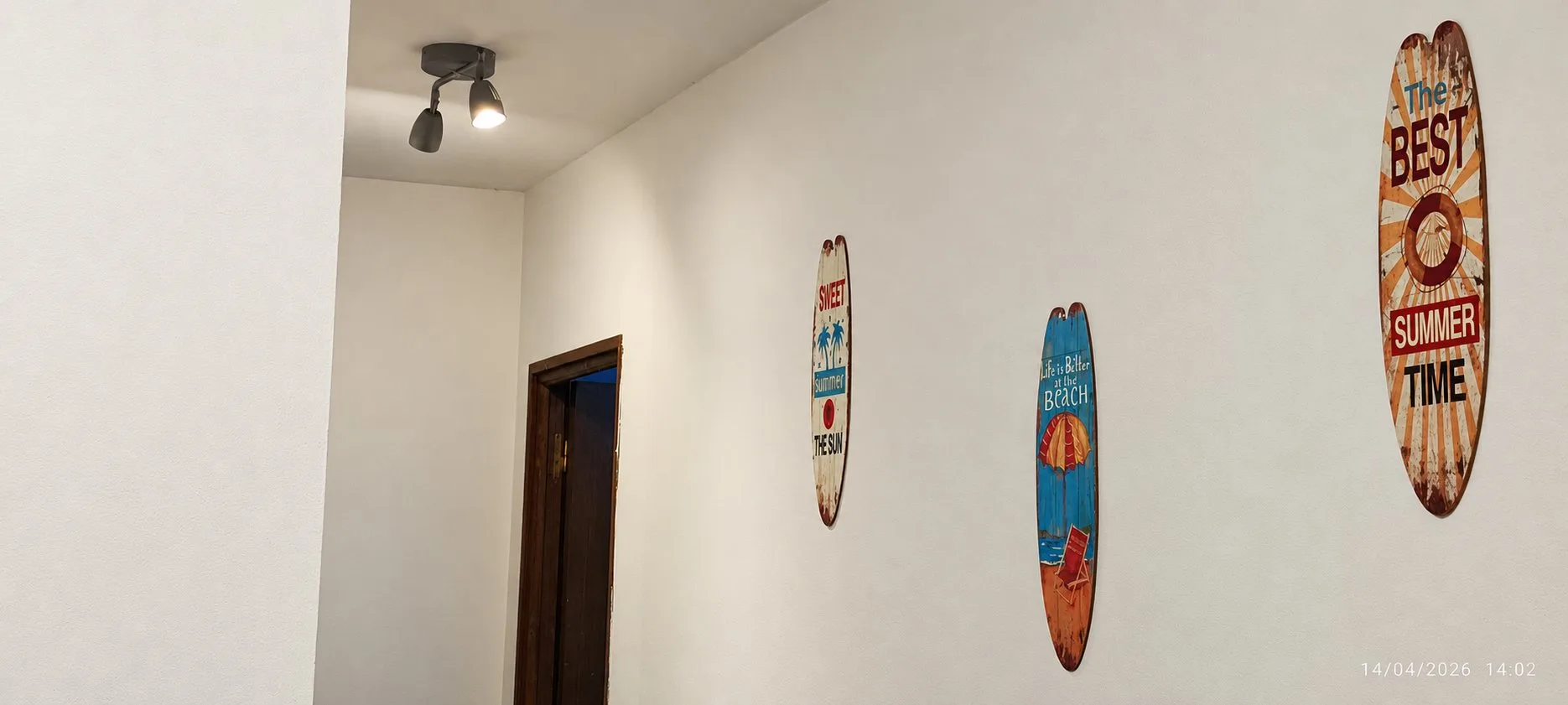 Couloir du gîte Jardin avec une porte sombre et des planches de surf décoratives accrochées au mur.