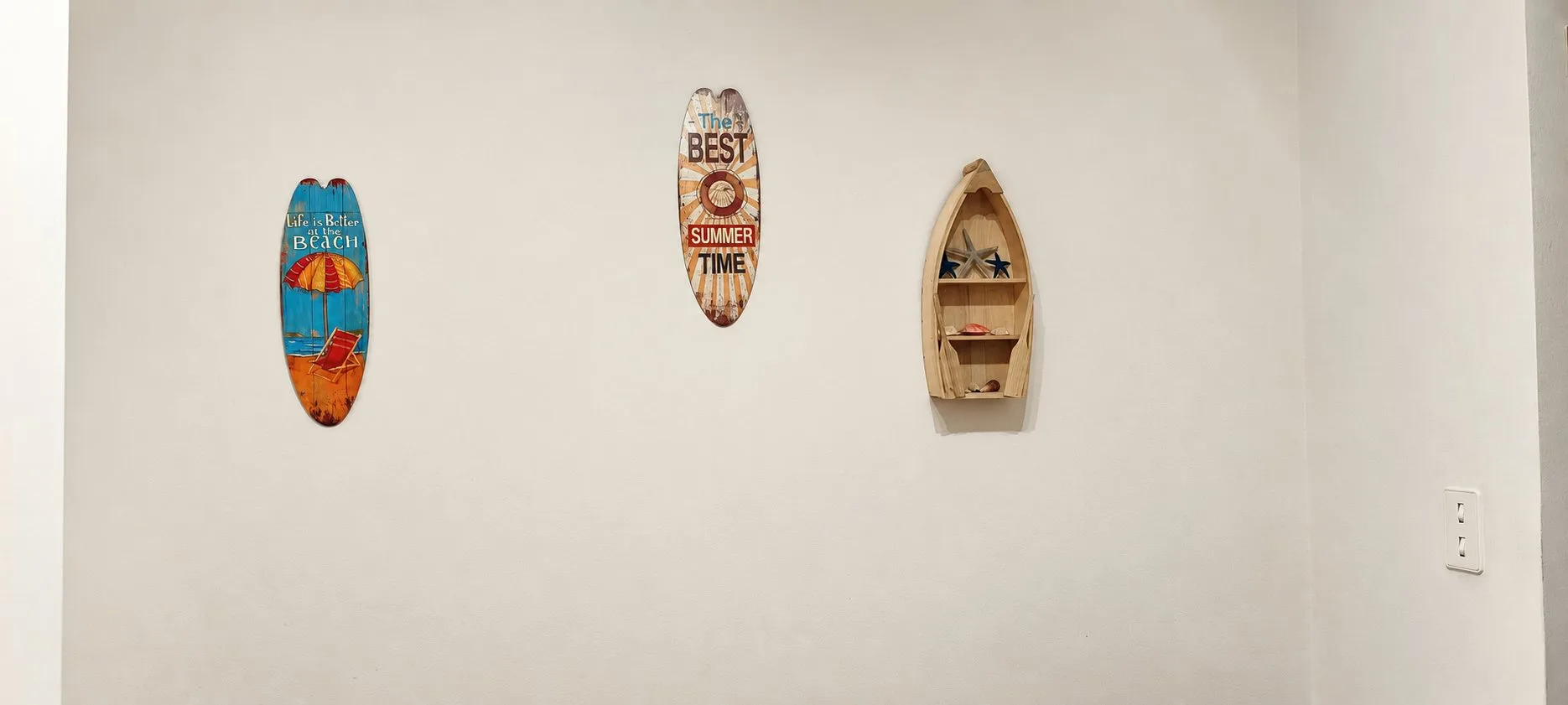 Trois planches de surf et une petite barque décoratives accrochées à un mur blanc du gîte Jardin.