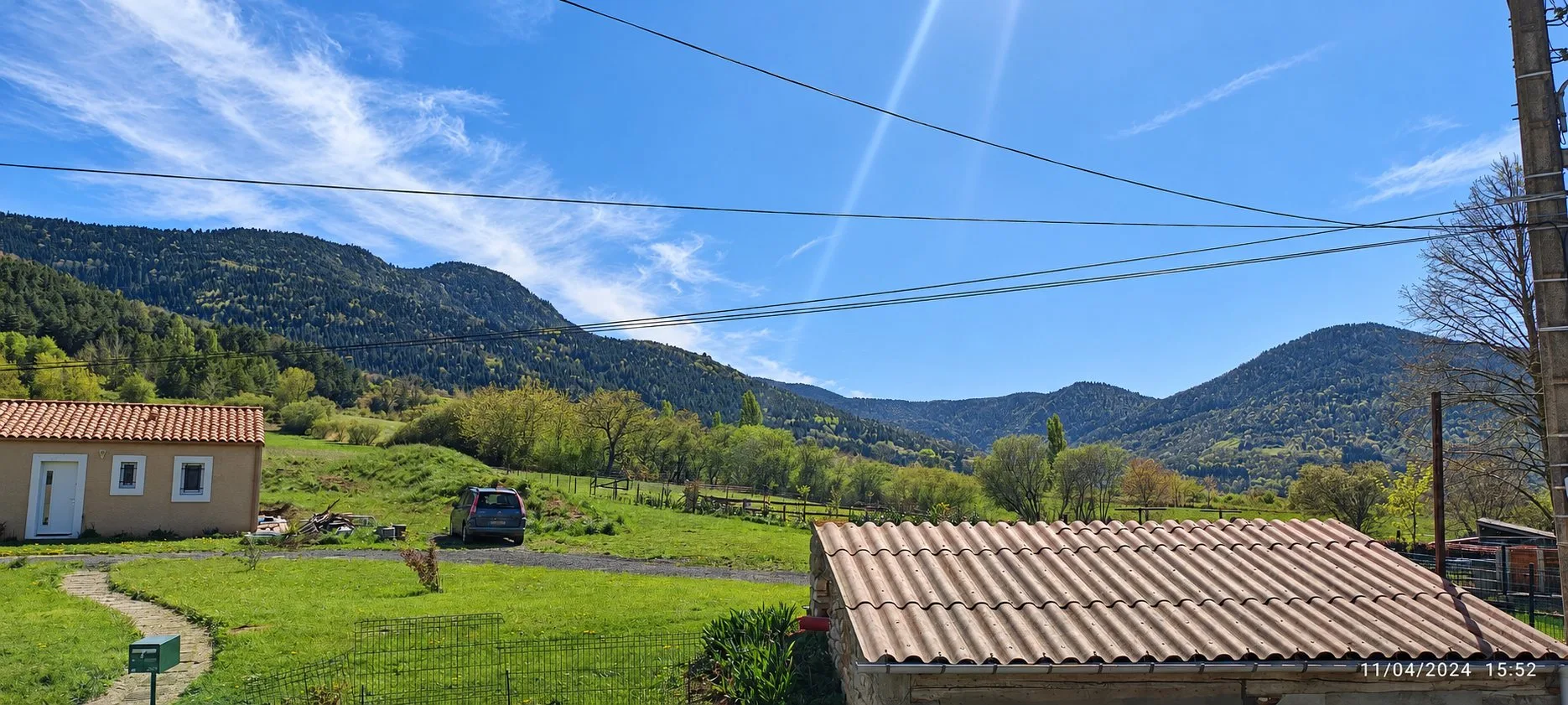 Vue depuis le gîte Terrasse sur la prairie, une maison au toit de tuiles et les montagnes boisées.