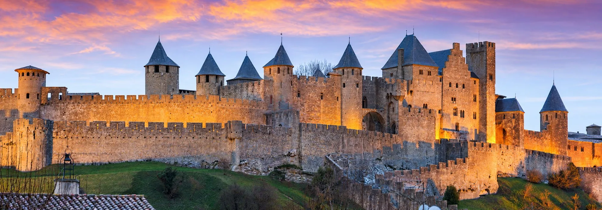 Les remparts et les tours de la cité de Carcassonne éclairés à la tombée de la nuit.