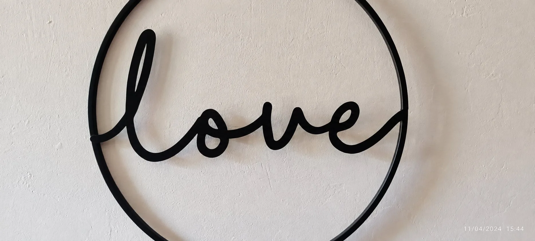 Gros plan sur un cercle en métal noir formant le mot « love », accroché à un mur blanc.