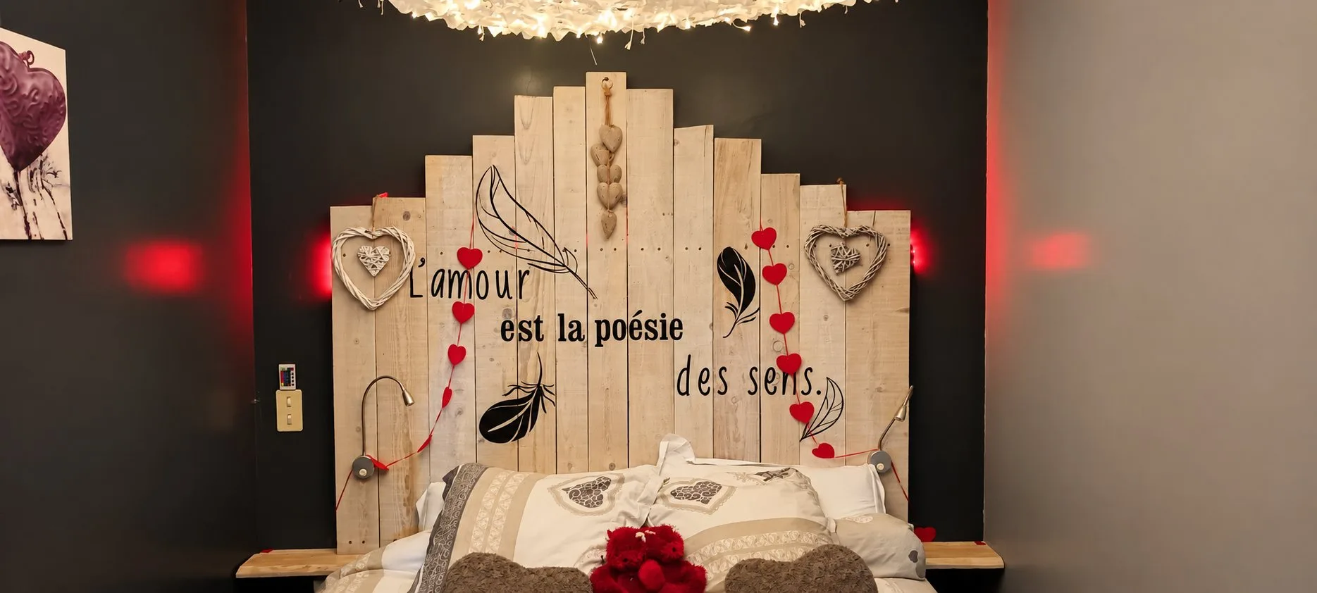 Tête de lit en bois de palette portant l'inscription « l'amour est la poésie des sens », avec des cœurs et des plumes.