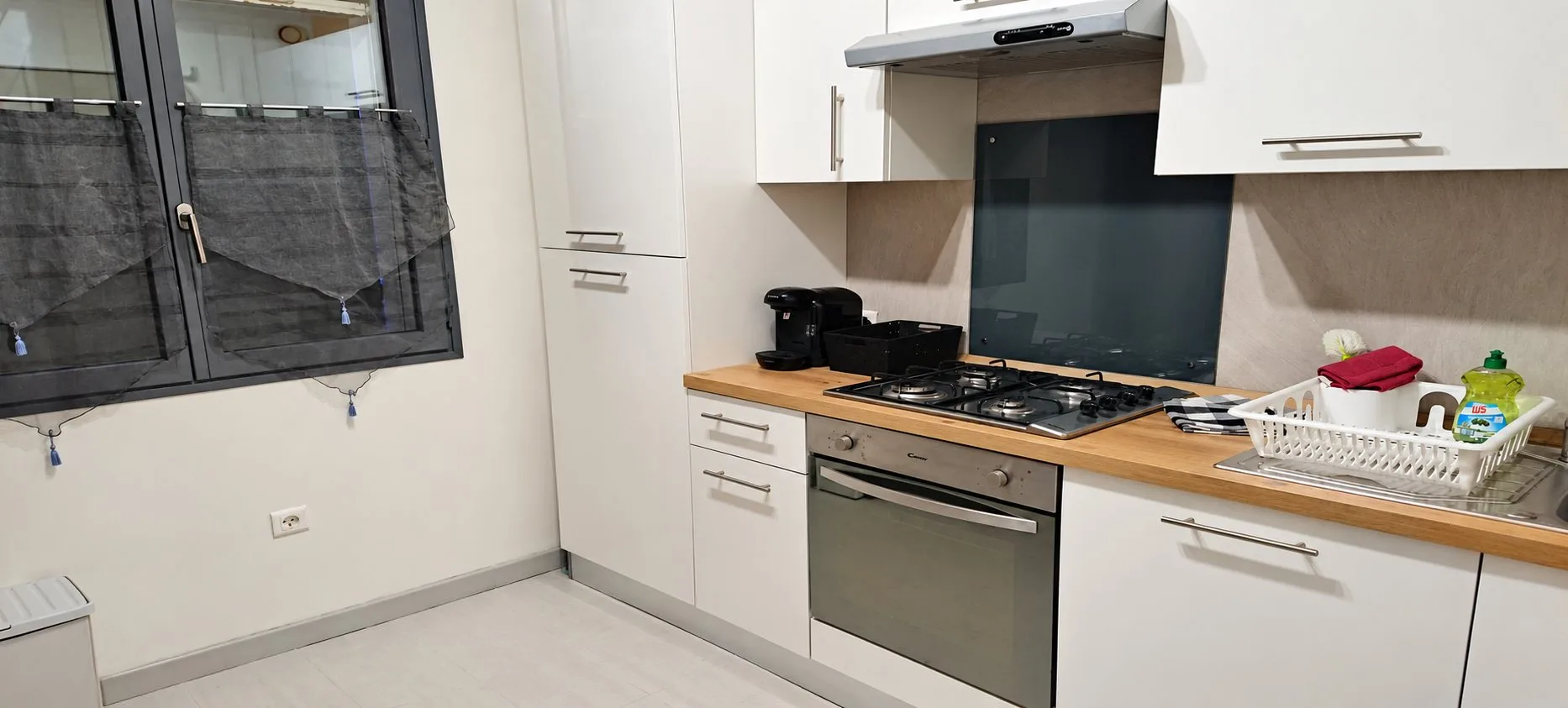 Cuisine de Piccolove avec meubles blancs, plan de travail en bois, plaque de cuisson, four et cafetière.