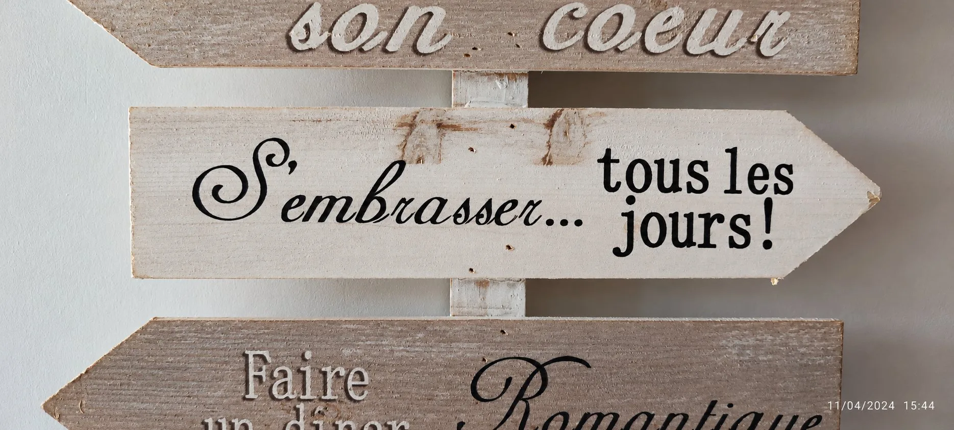 Gros plan sur des flèches en bois peint portant des messages romantiques, accrochées à un mur blanc.