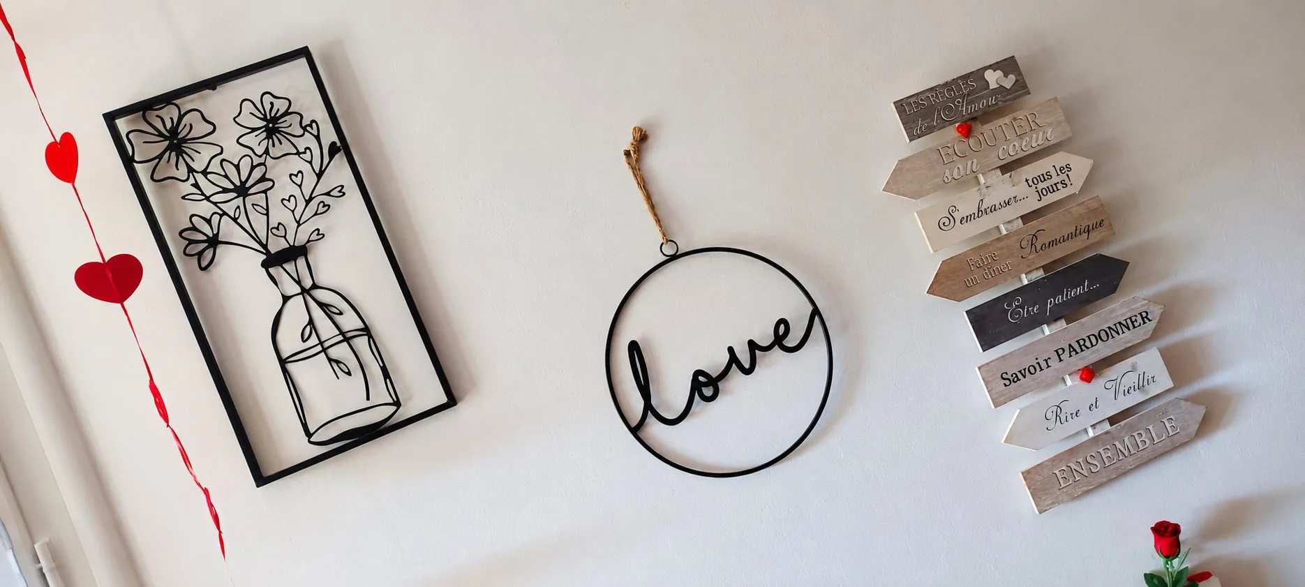 Mur blanc de Piccolove orné d'un cadre métallique de fleurs, d'un cercle « love » et de flèches en bois portant des messages.