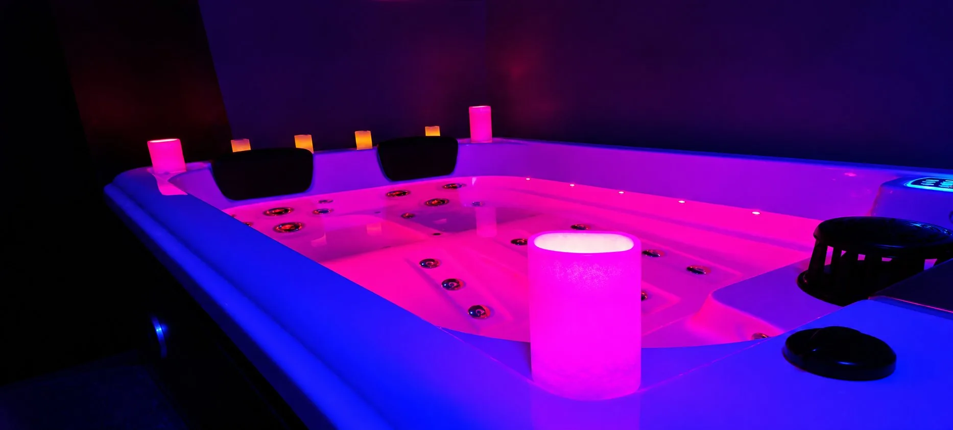 Spa privatif de Piccolove éclairé en bleu et rose, avec des bougies sur le rebord.
