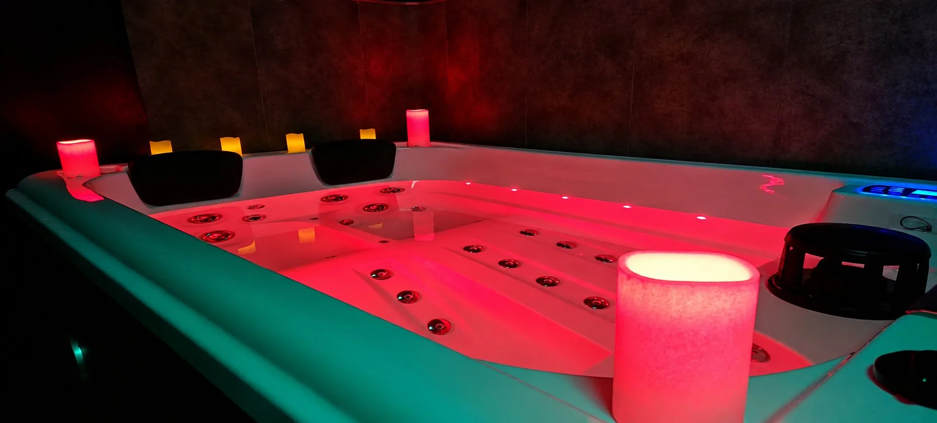 Spa privatif de Piccolove éclairé en rouge, avec des bougies sur le rebord et des appuie-tête noirs.